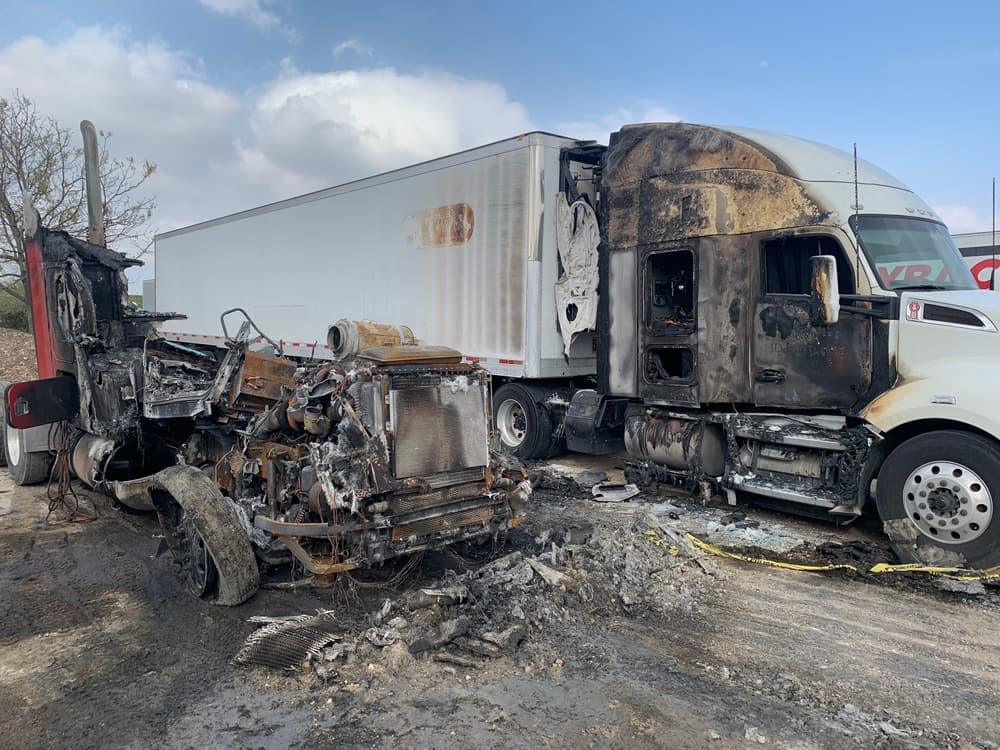 Burnt wreckage of two semi-trucks after a collision, highlighting the devastation of trucking accidents.