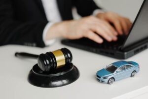 A lawyer typing on a laptop with a gavel and a toy car nearby.