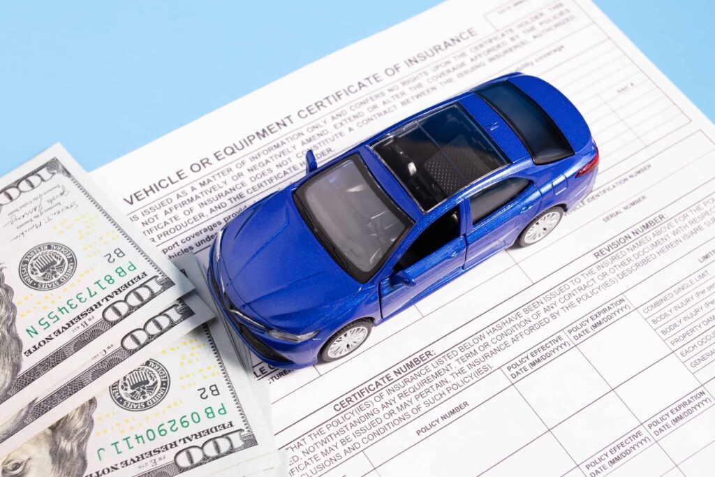 Blue car model placed on auto insurance certificate with cash, representing vehicle insurance coverage and claim compensation