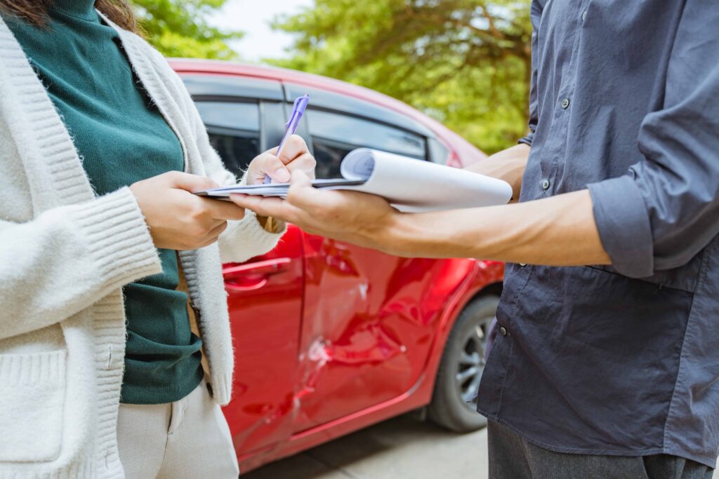 Driver completing an accident report after a car crash, documenting damage to a red vehicle for an insurance claim